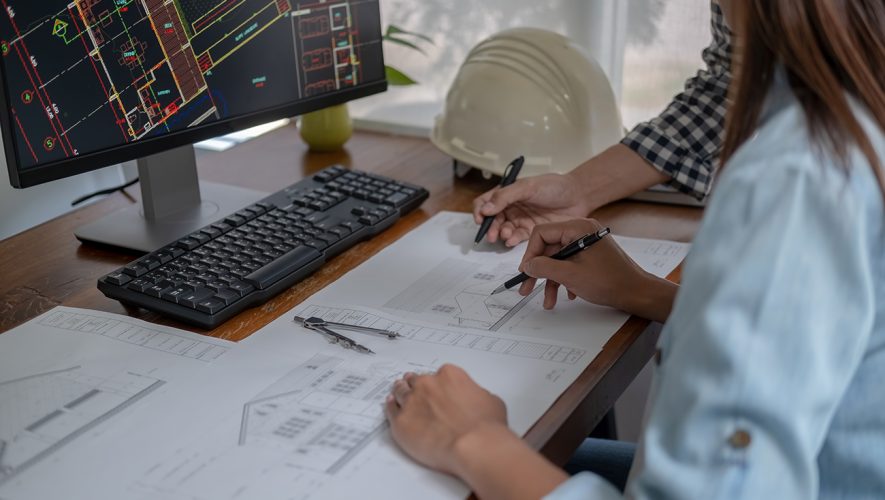 Engineers discuss a blueprint while checking information on a tablet computer in a office.